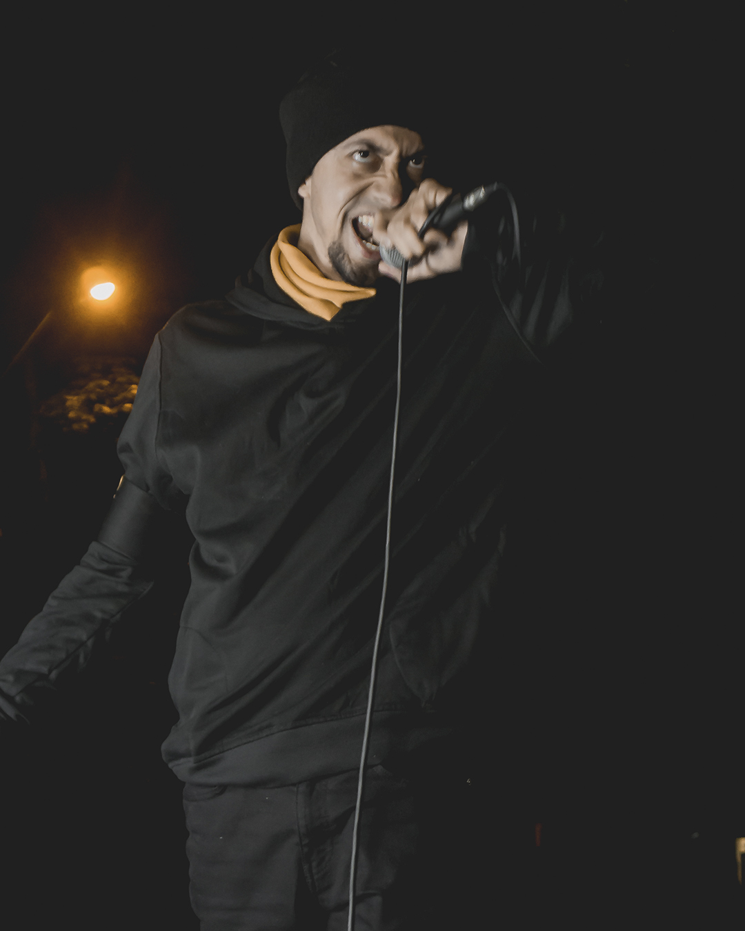Foto de vocalista de la banda ground of chaos sostienendo un microfono en la noche con ropa negra